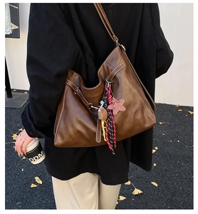Detail of dark brown leather tote bag featuring contrast stitching and star tassel charm