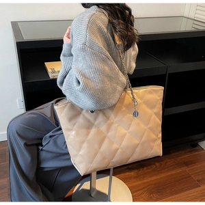 Close-up of beige quilted tote bag with metal chain strap worn by a sitting model