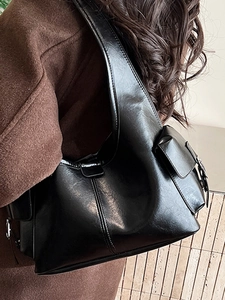 Glossy black underarm tote bag with metallic buckle and side pocket detail on brown coat