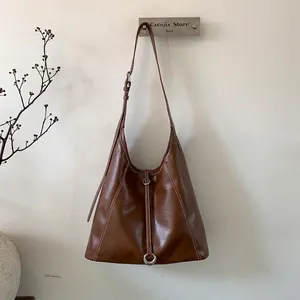 Detail of dark brown tote bag featuring white contrast stitching and silver metal ring