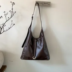 Detail of dark brown tote bag showing contrast stitching and metal ring decoration