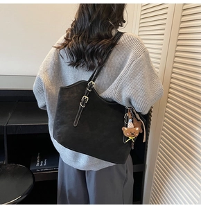 Detail of adjustable shoulder strap and cute bear charm on a black leather tote bag