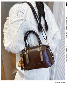 Detail view of dark brown leather Boston bag with wooden beads on a white knit sweater