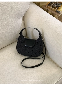 Détail d'un sac à bandoulière noir à pois sur un canapé blanc à texture bouclée