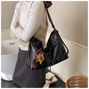 Detail of black tote bag with white contrast stitching and a small brown bear charm