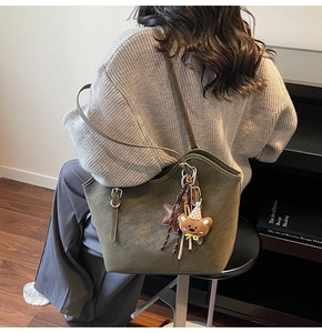 Detail view of large olive green suede tote bag with decorative straps and plush charms