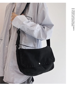 Detail of black canvas messenger bag featuring a silver metal button and flap closure