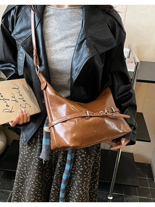 Detail of a brown glossy PU shoulder bag with adjustable buckle strap and retro metal eyelets