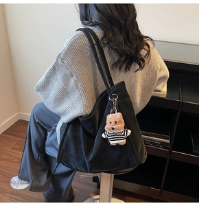 Close-up of black suede tote bag with cute teddy bear charm in indoor setting