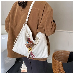 Detail view of cream-white leather tote bag with cute brown bear charm on soft PU material