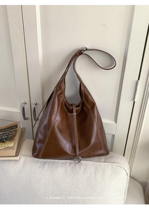 Detail of a brown Hobo tote with contrast stitching and metal ring on a cream sofa