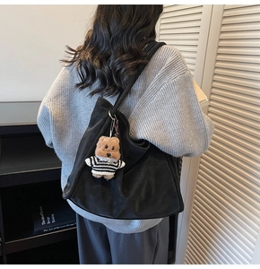 Detail of black tote bag with cute teddy bear charm on shoulder of model in grey sweater