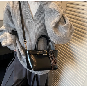 Detailed view of black glossy crossbody bag with decorative buckles and a brown charm