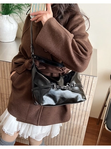 Close-up of black glossy hobo bag with silver buckle strap detail and metallic highlights