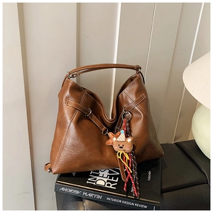 Brown faux leather hobo tote bag with a cute bear charm and tassel detail on a desk