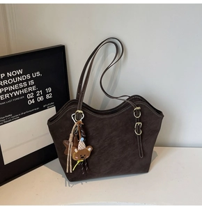 Detail of dark brown suede tote bag with golden buckle and cute bear pendant