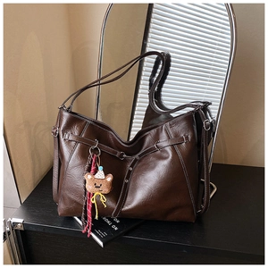Detail of dark brown leather tote with silver rivets and cute bear charm accessory