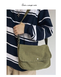 Olive green canvas messenger bag worn by model over a blue and white striped shirt