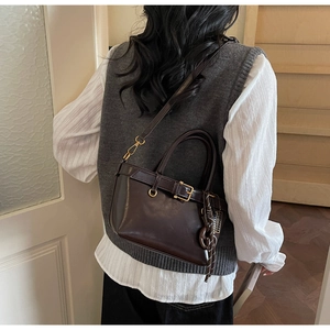 Detail of vintage brown crossbody bag with gold buckle and woven charm on a model