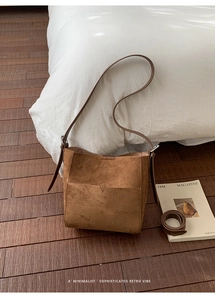Détail d'un sac seau en daim marron avec bandoulière réglable sur un sol en bois massif
