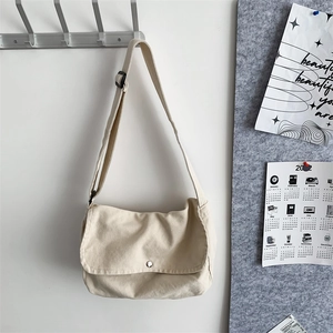 Detail of off-white canvas crossbody bag with silver magnetic snap and adjustable strap