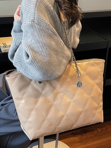 Retro quilted beige tote bag with chain strap shown on a model in a minimal setting