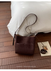 Détail du sac seau en daim marron foncé avec poche à coupe en V sur fond de parquet