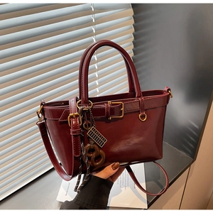 Detail showing deep red PU leather texture, golden hardware and creative bag charms