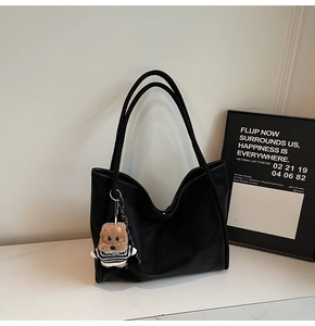 Detail view of a black leather tote bag with a cute bear charm on a white marble surface