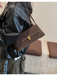 Dettaglio della borsa baguette in camoscio marrone scuro con fibbia dorata su giacca