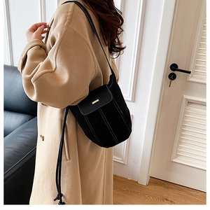 Detail of black crossbody bag with contrast stitching and gold metal bar on camel coat