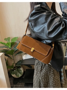 Dettaglio borsa baguette in pelle scamosciata marrone con fibbia dorata portata a spalla