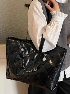 Glossy black quilted tote bag with chain strap shown on model for chic winter style