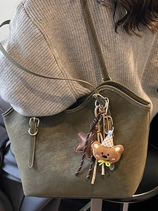 Moss green faux suede tote bag with bear charm and white stitching on a gray sweater