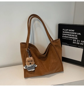 Detailed side view of the brown leather tote bag featuring a cute teddy bear charm