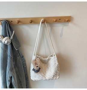 Détail d'un sac cabas en peluche blanche avec pendentif ours brun sur un cintre en bois