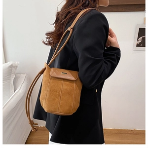 Close-up of tan suede bucket bag with leather patchwork and metal bar on black blazer