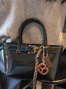 Chic black glossy handbag with vintage gold charms on a model in gray sweater