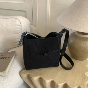 Detail of minimalist black suede bucket bag with adjustable strap on a cozy sofa
