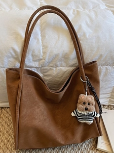 Retro brown large capacity tote bag with cute plush bear pendant on white soft bedding