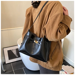 Détail du sac bandoulière noir en cuir avec fermoir doré et cordon sur une veste marron