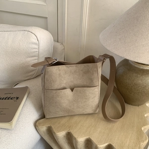 Close-up of a beige suede bucket bag on a wooden table with soft lifestyle background