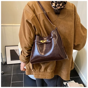 Détail du sac bandoulière en cuir café avec boucle dorée vintage porté par un mannequin