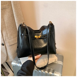 Détail du sac cabas en cuir noir avec boucle dorée sur une valise argentée