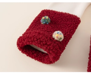 Close-up of red fleece cuffs with colorful pom-poms on a white children's sweatshirt