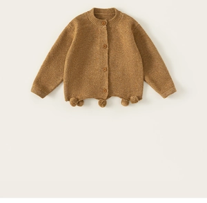 Close-up of knit baby cardigan with wooden buttons and decorative hanging pom-poms