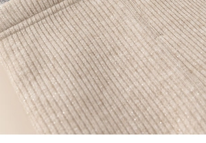 Macro shot of warm apricot ribbed knit fabric with subtle metallic shimmer and soft texture