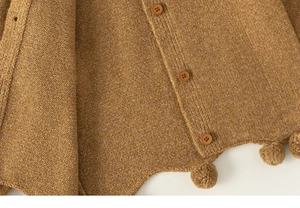 Detail view of mustard yellow knit cardigan with wooden buttons and pom-pom trim