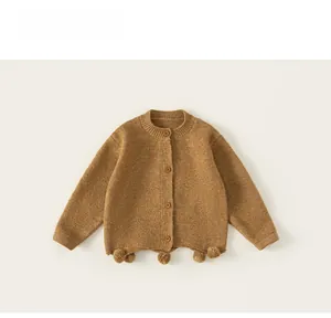 Close-up of caramel knit cardigan with brown buttons and textured pom-poms on the hem