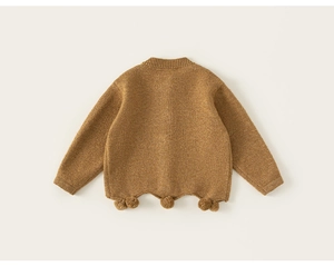 Detail shot of brown knit children sweater with textured scalloped hem and pom-poms